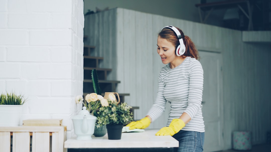 services-03 Good-looking girl is dusting table at home and listening to pop music through headphones, singing and dancing with happy face. Millennials, household and interior concept.
